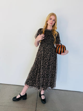 Woman in a black floral dress holding a striped bag against a white background
