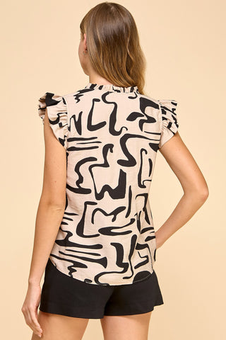 A woman with light brown hair wears the Shop-Peppermint ABSTRACT PRINT V-NECK TOP TAN, featuring ruffled sleeves and black abstract patterns, paired with black shorts. She faces away from the camera against a plain beige background. Made in the USA.