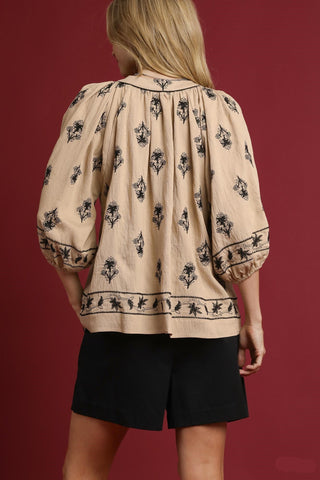 Woman wearing a beige blouse with black floral patterns and black shorts on a red background