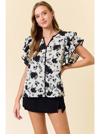 Woman wearing a black and white floral blouse with ruffled sleeves on a beige background