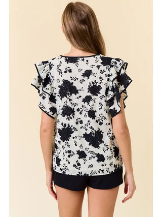 Woman wearing a black floral blouse with ruffled sleeves on a beige background