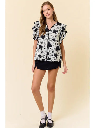 Woman wearing a black and white floral blouse with black shorts on a beige background