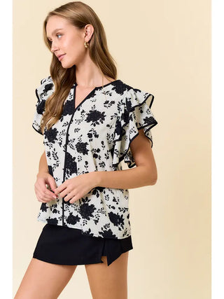 Woman wearing a black and white floral blouse with ruffled sleeves on a beige background