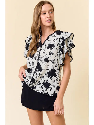 Woman wearing a black and white floral blouse with ruffled sleeves on a beige background