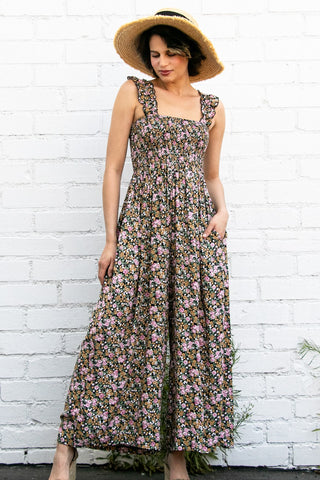 Woman wearing a floral dress and straw hat against a white brick wall.