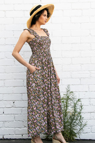 Woman wearing a floral dress and straw hat against a white brick wall.