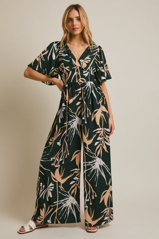 Woman wearing a long, dark green dress with a floral pattern on a beige background