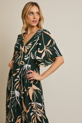 Woman wearing a dark green dress with leaf pattern on a beige background