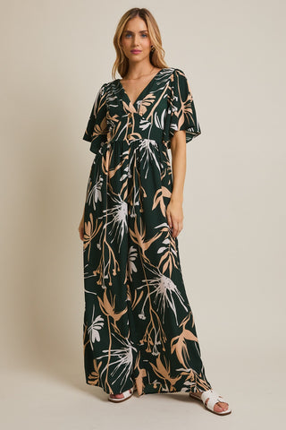 Woman wearing a long, dark green dress with a floral pattern on a beige background