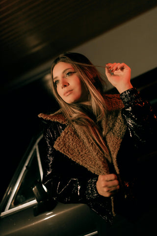 Woman in a dark coat standing next to a car at night